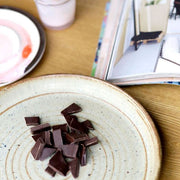 Round dinner plate on a wooden table with little pieces of dark brown chocolate on it.