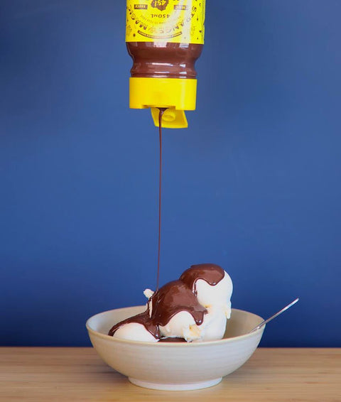 Chocolate sauce dripping from a yellow plastic squeeze bottle onto vanilla ice-cream.