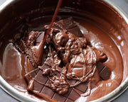 Multiple blocks of dark brown chocolate melting in a large silver pot.