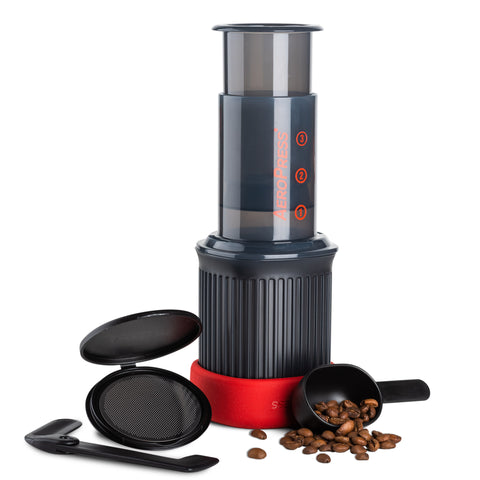 Assortment of Aeropress products. Featuring a long black Aerorpess GO. Accompanied by a circular black aeropress filter.